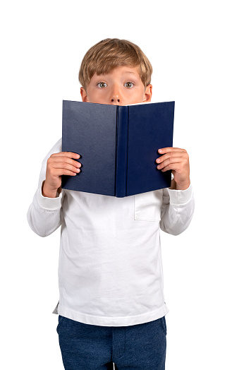 School boy standing with book in hands and eyes wide open, looking at the camera, isolated over white background. Concept of education, career, idea and creativity