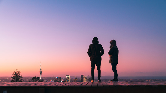 Two young man standing on viewing desk at Mt Eden enjoying city lights after sunset of Auckland Skyline.