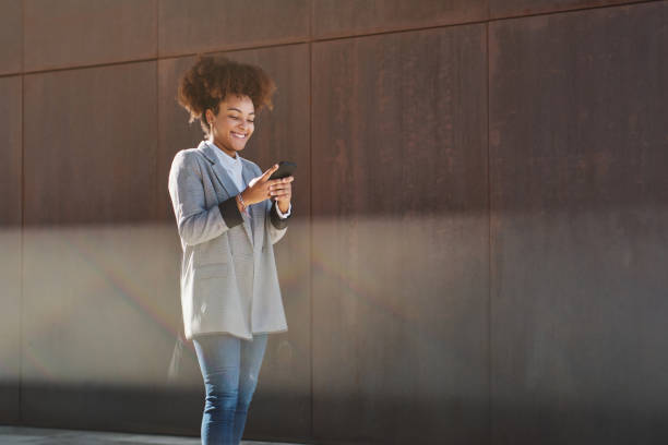 istock Smiling black woman browsing smartphone on street 1582313604