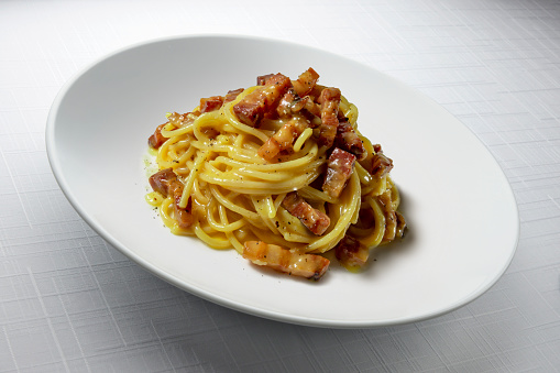 Modern design soup plate with spaghetti carbonara isolated on table with white tablecloth