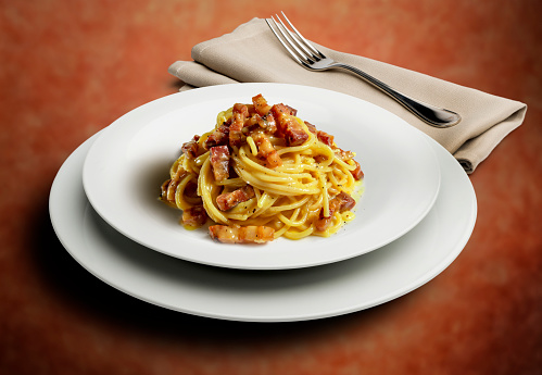 Deep plate with spaghetti alla carbonara with napkin and fork solated on a speckled background