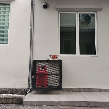 locked red gas tank behind a house under the window.