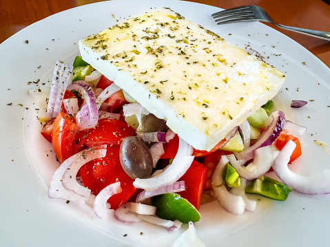 Healthy greek salad of fresh vegetables with tomatoes, pepper, cucumbers, red onions, olives, feta cheese in plate on the table. Healthy food, vegetarian dieting. Tavern in Naoussa, Paros Island, Greece.