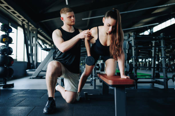 istock Dynamic Training Male Personal Trainer Helps Woman with Gym Workout 1582360794