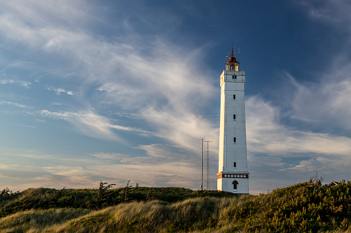 white lighthouse at sunset with white clouds and blue sky behind
