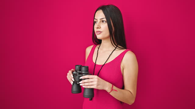 Young beautiful hispanic woman lifeguard using binoculars with relaxed expression over isolated red background