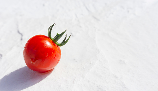 Tomato with water droplets on a white stucco board.