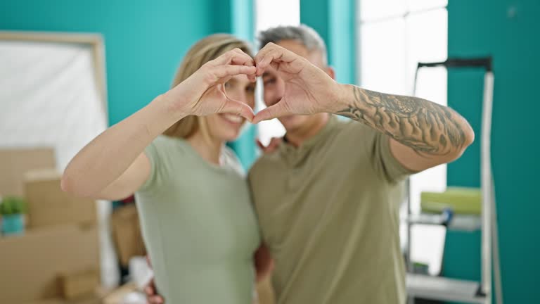 Man and woman couple hugging each other doing heart gesture at new home