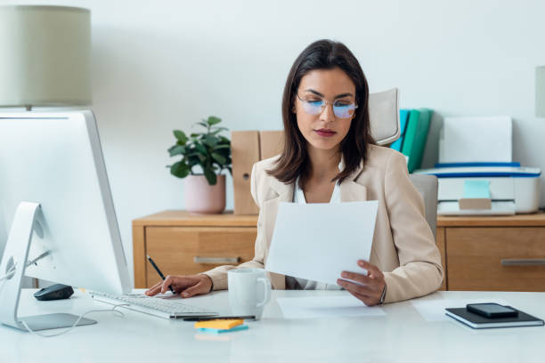 istock Elegant smart business woman working with computer while reading some notes in the office 1582432804