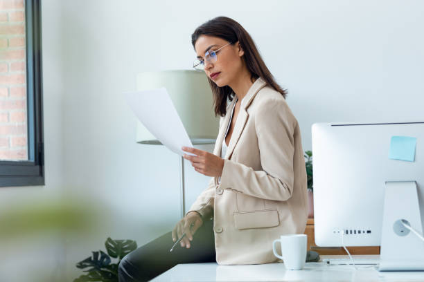 istock Elegant beautiful businesswoman working while reading some documents sitting on the desk at office 1582433008