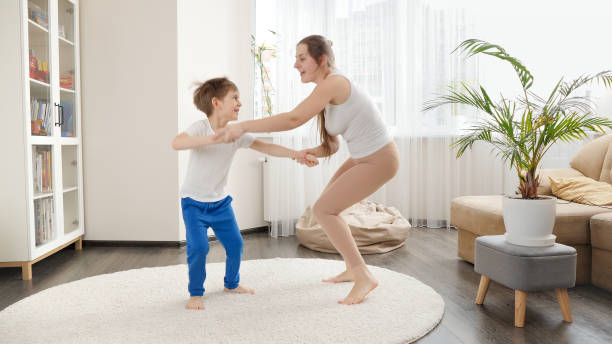 Happy smiling mother playing and dancing with her little son in living room at home. Family having fun together, listening music, active lifestyle, parenting and child development Happy smiling mother playing and dancing with her little son in living room at home. Family having fun together, listening music, active lifestyle, parenting and child development. baby boy dancing with his mommy stock pictures, royalty-free photos & images