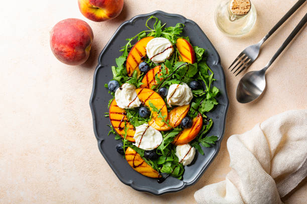 Grilled peach salad with arugula, mozzarella buffalo cheese, blueberries, balsamic sauce. Directly above, beige background, copy space.