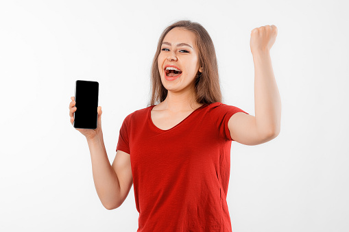 Online Win. Portrait of overjoyed brunette girl making winner gesture and showing blank mobile phone screen, standing over white background