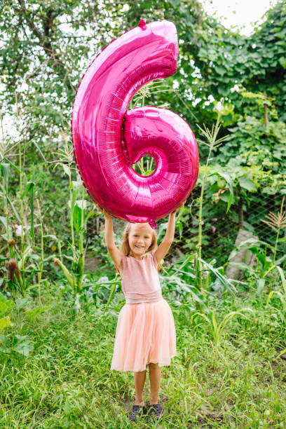 happy girl holding a balloon on her sixth birthday in the backyard. funny emotional child with pink balloon in the garden. 6 six years old, 6th birthday party celebration balloon. - circa 6th century imagens e fotografias de stock