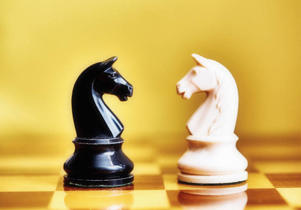 istock Conflict and rivalry: black and white chess knights face off against each other 1582523663