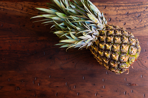 High angle view of pineapple fruit over a rustic wooden table in the kitchen at home. Delicious healthy food to eat as dessert at home .Image made with a full frame camera and 50 mm lens f-stop 1.4