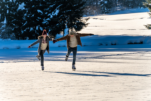 Couple ice skating on frozen lake while holding hands during winter day.