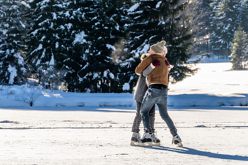 Couple ice skating while embracing on frozen lake.