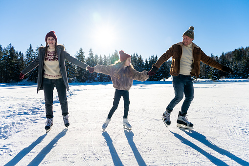 Family ice skating on frozen lake while holding hands during winter day.