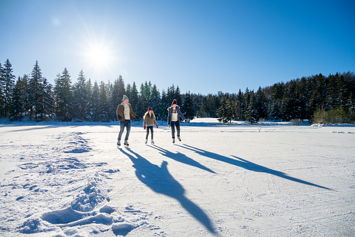 Family ice skating on frozen lake against forest during winter day.