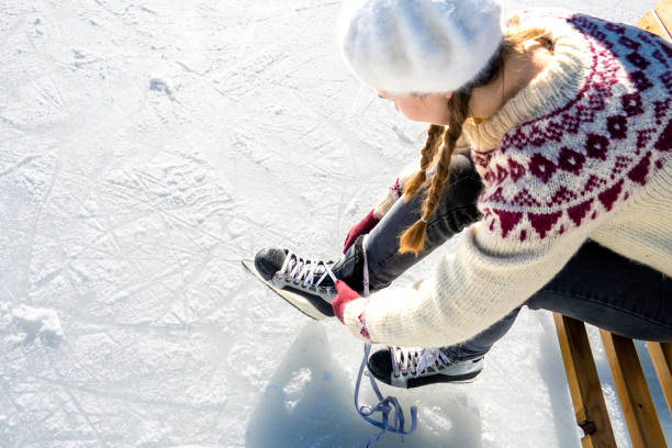 A close-up of a girl's hand holding ice skates at a skating rink.