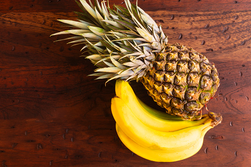 High angle view of fresh pineapple with bananas over rustic wooden table in the kitchen at home.Healthy fruits to eat.Image made in studio with a full frame camera and 50 mm lens f-stop 1.4