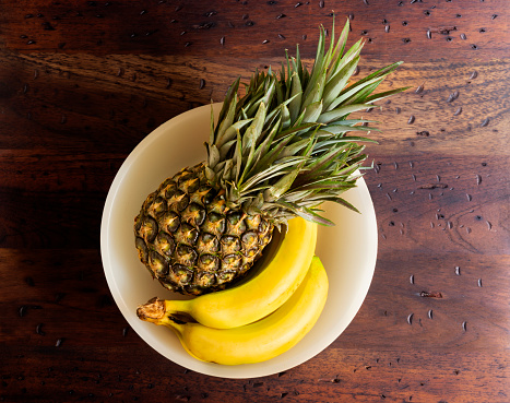 High angle view of fresh pineapple with bananas over rustic wooden table in the kitchen at home.Healthy fruits to eat.Image made in studio with a full frame camera and 50 mm lens f-stop 1.4