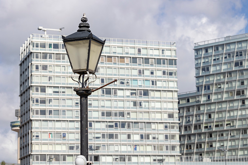 An old street lamp on a pole against the background of modern buildings.