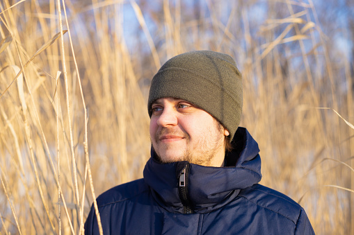Male man on high dry reeds. European caucasian white smiling man, positive emotion. lifestyle portrait of looking away male. Winter hiking, leisure activities.