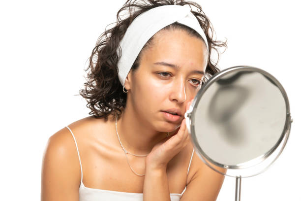 disappointed etnic woman without makeup looking herself in the mirror on a white background stock photo