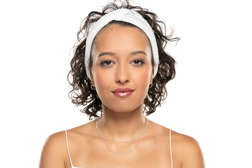Young dark skinned woman with makeup and headband posing on a white studio background
