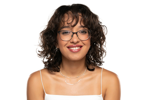 Young dark skinned smiling woman with makeup, glasses  and wavy hair posing on a white studio background