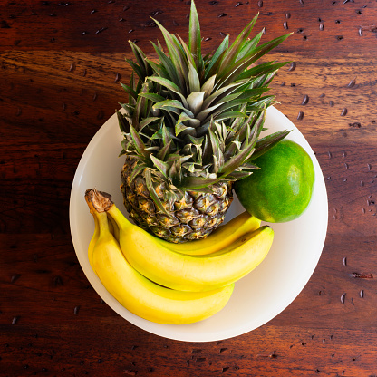 High angle view of fresh pineapple fruit with bananas a one avocado over a rustic wood table in the kitchen at home. Image made in studio with a full frame camera and 50 mm lens f-stop 1.4