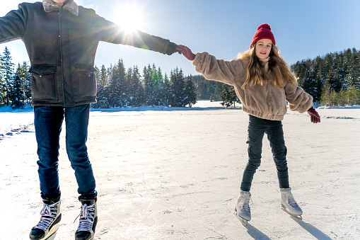 Grandfather holding hands to granddaughter while ice skating on frozen lake.