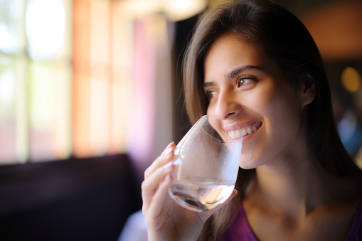 Happy woman drinking water looks at side in a restaurant