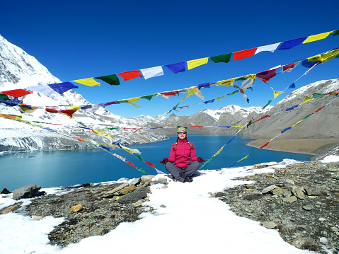 Woman sitting in meditation in the mountains in Nepal. Tilicho Lake and Tibetan prayer flags are in the background.