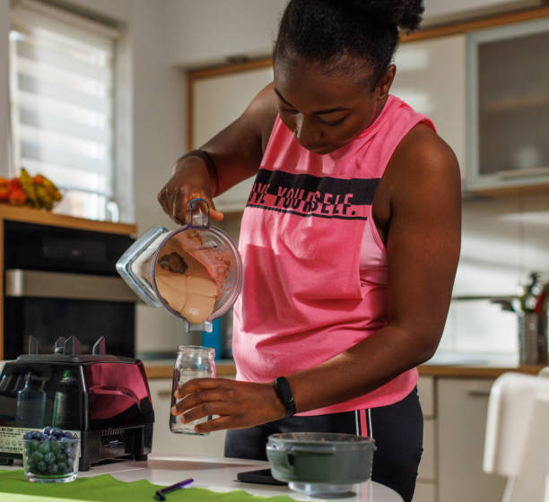 A Black Woman Pouring A Protein Shake Into A Glass