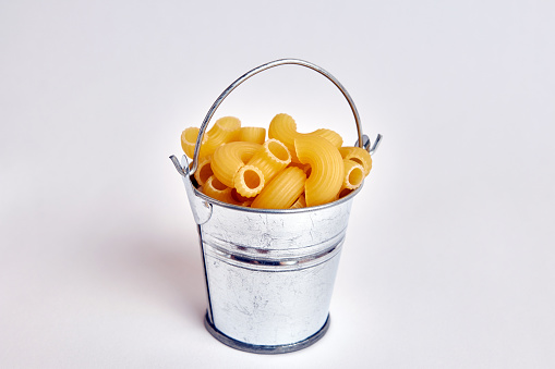 Miniature metal bucket filled with pasta on a white background.