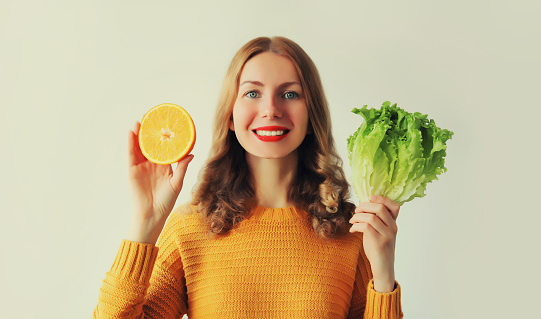 Nutrition, healthy food, diet and vegetarian concept. Happy smiling young woman with slices of orange fruits and green lettuce on white background