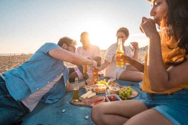 istock Multiracial Couples Enjoying Beer And Snacks on Sunset Beach Picnic 1582604904