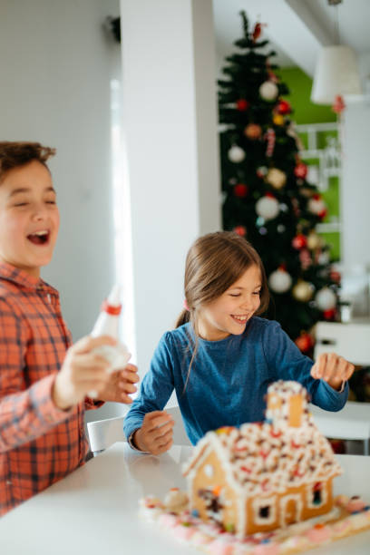 istock Two children decorating the gingerbread house at home 1582618112
