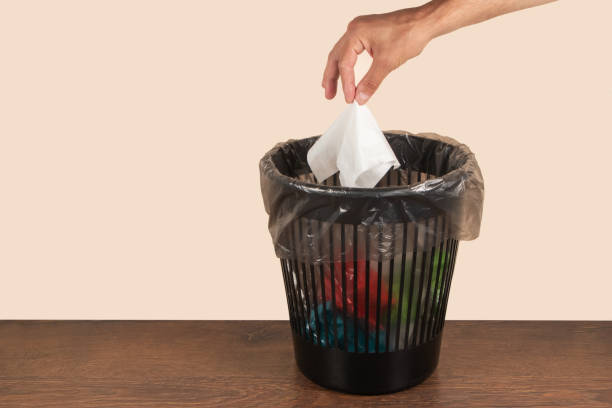 istock Man putting paper tissue into trash bin on light brown background 1582646245