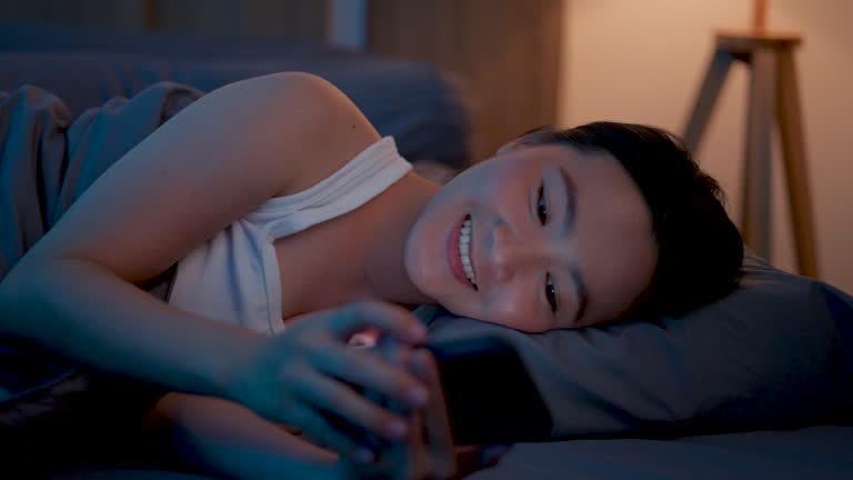 Asian woman happy smiling using smart phone for searching, shopping online or surfing social media in bed room at night.