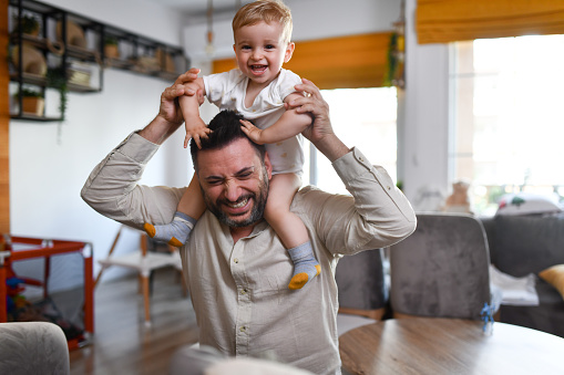 Father Carrying Baby Son On Shoulders While Enduring Hair Pulling