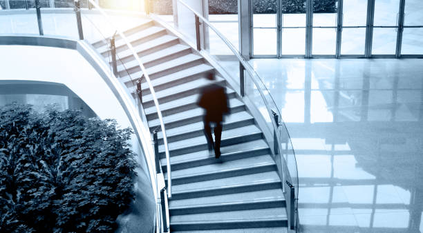 istock Single business man walking up stairs in office building 1582681752