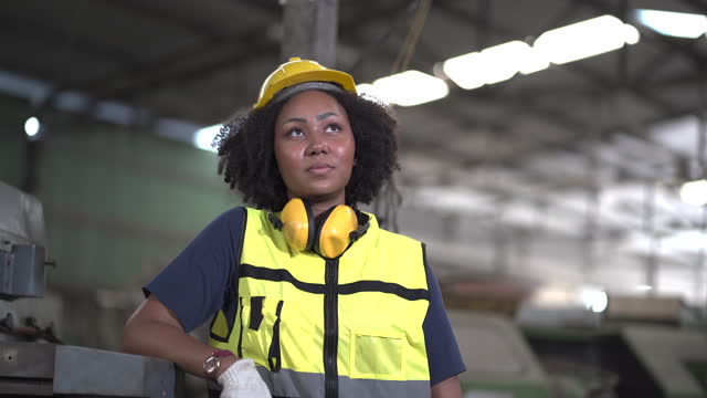 tired African American mechanical engineer worried standing by old machine in factory. black labor worker woman bored work in warehouse . female unhappy in workplace looking up