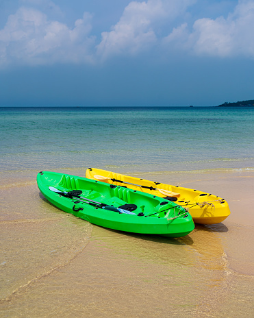 Two kayaks on the beach. turquoise water. One green kayak, the other yellow kayak. Paddles in kayaks. Cambodia