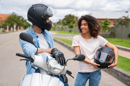 Happy Latin American man picking up his girlfriend on his motorcycle and going for a ride wearing helmets
