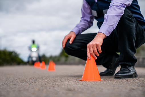 Close-up on a motorcycle driving instructor putting traffic cones on the ground while teaching a lesson