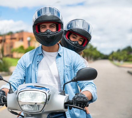 Happy Latin American couple going for a ride on their motorcycle and looking at the camera